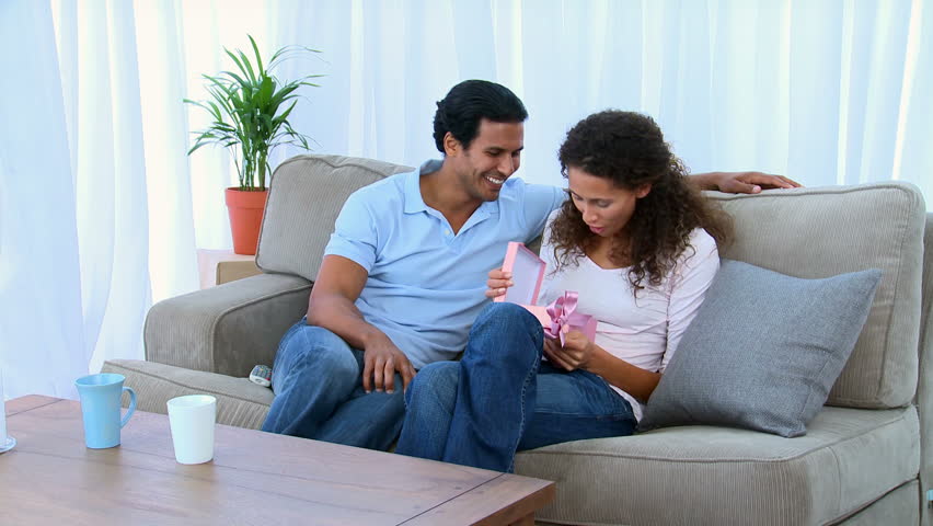 Happy woman opening the gift that was offered by her husband on the sofa at home