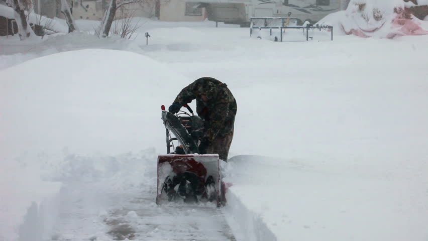 Man walks away from a snow blower in deep snow. Deep snow blizzard. Snow blowing in strong wind in sub freezing weather. Winter time hazard and climate nature.