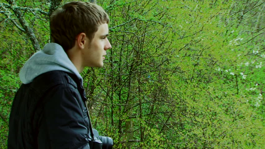 A young man with a camera photographing beautiful green scenery.