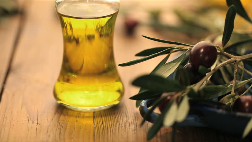 bottle of olive oil with olives rolling in foreground