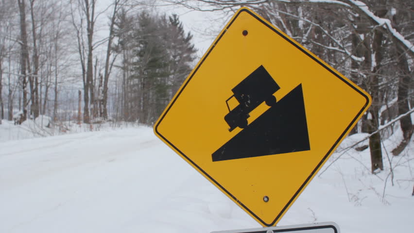 Steep hill sign. Winter. Yellow, diamond shaped sign warns of steep hill ahead. Light snow falling. Winter road in rural Ontario, Canada. 