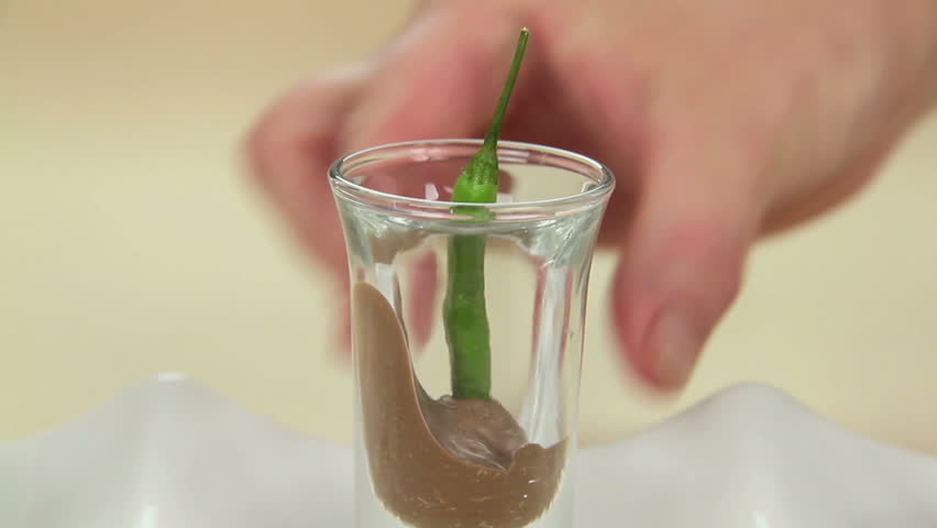Placing chillies dipped in chocolate in shot glasses in a row on a tray. 