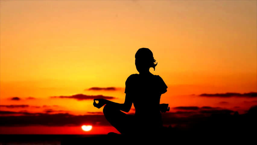 Silhouette of woman meditating during sunset