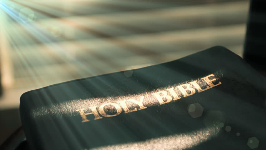 Sunlight filters through window shades and casts a beam of light the word Holy Bible. Flare added for drama.