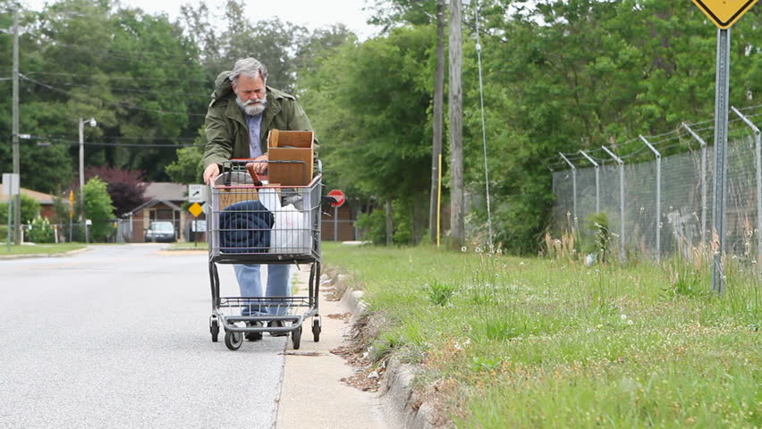 Homeless veteran pushes a shopping cart that holds his belongings down the side of the street.