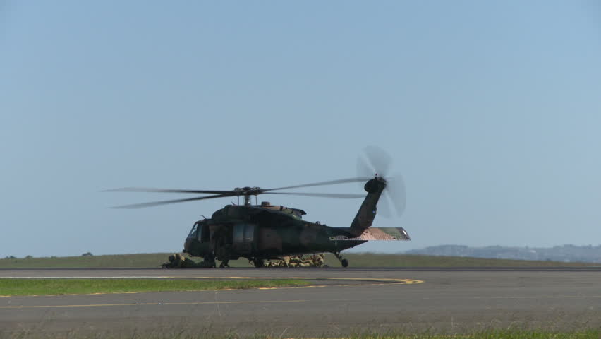 A blackhawk military helicopter takes off after dropping off a squad of soldiers.  Soldiers run as helicopter takes off