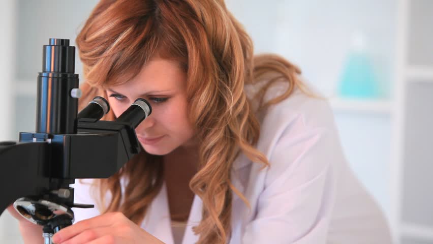 Blond-haired scientist woman looking through a microscope in a laboratory