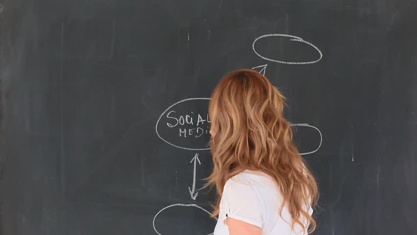 Cute blond-haired teacher drawing a scheme on a chalkboard