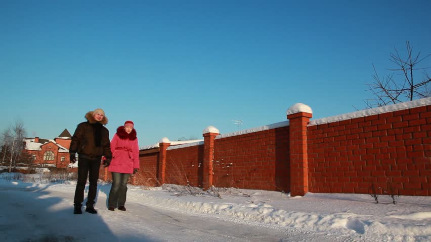 beautiful young woman in pink jacket and man in glasses walking outdoors at winter, house