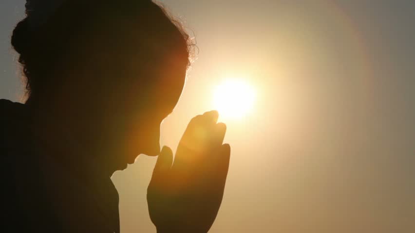 Silhouette of woman head with sunshine behind, she is praying