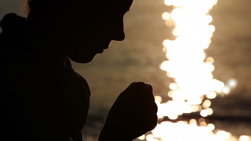 Silhouette of woman head with sunshine reflected in water behind, holding two fists together