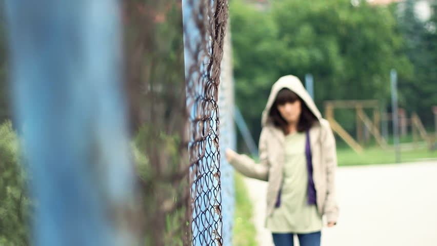 Sad beautiful woman by chain-link fence, outdoors 
