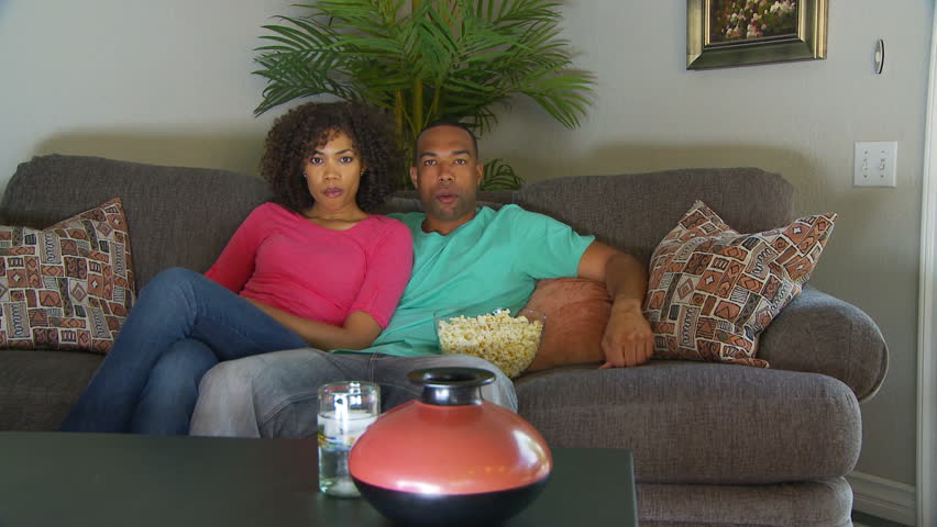 Couple watching movie on couch while eating popcorn