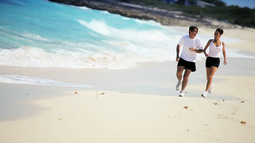 Attractive caucasian couple jogging along a beautiful tropical beach