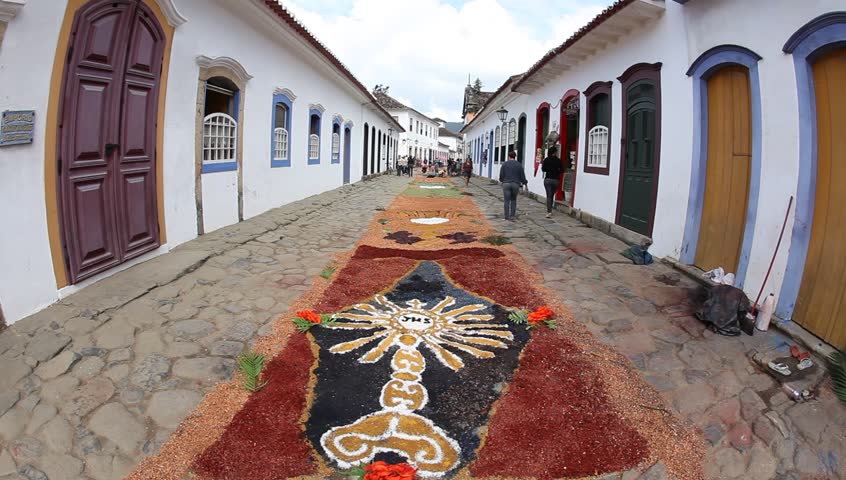 PARATY BRAZIL - JUNE 23: Pedestrians walk on cobblestone streets with tapestries made of colored sawdust, pigments, and flowers decorated by Catholics before the procession of Corpus Christi, June 23 2011 in Paraty, Brazil. 