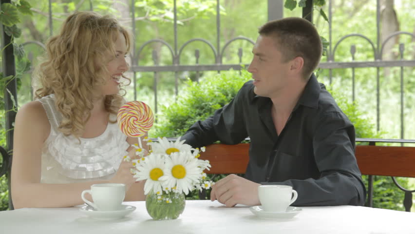 EDIT 2 CAMS Romantic young couple tasting big colorful lollipop, sitting in front of well-served table, flirting, smiling, communicating, young woman touching man's head. 