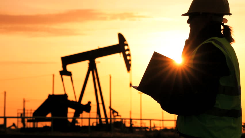 Female engineer with clipboard using a cell phone at the site of crude oil production