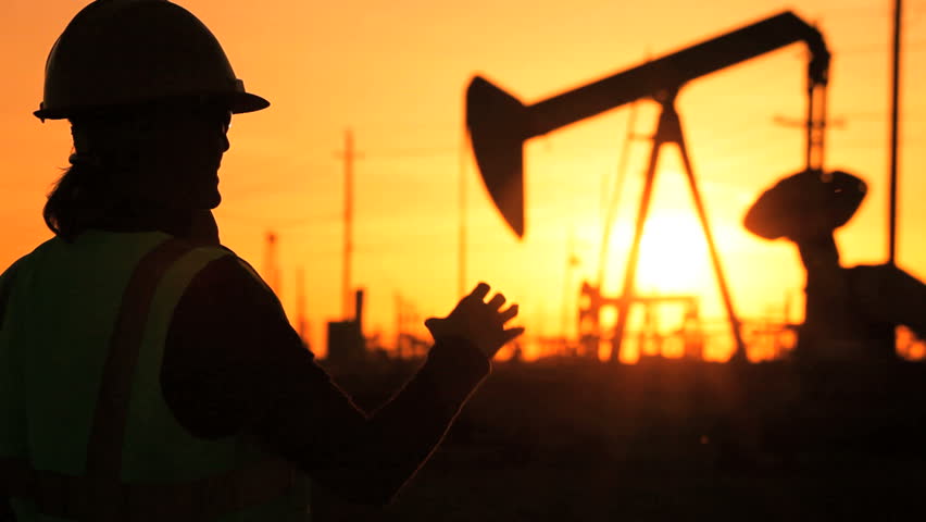 Female engineer using a cell phone at sunset at the site of a crude oil production farm
