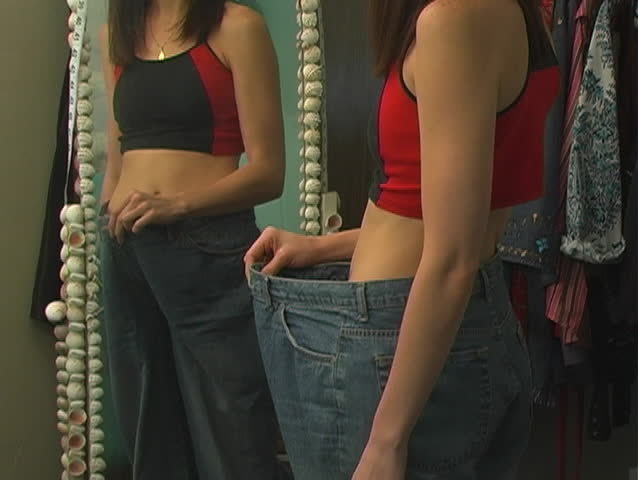 A beautiful young woman admires her weight loss progress.  Camera pans up.