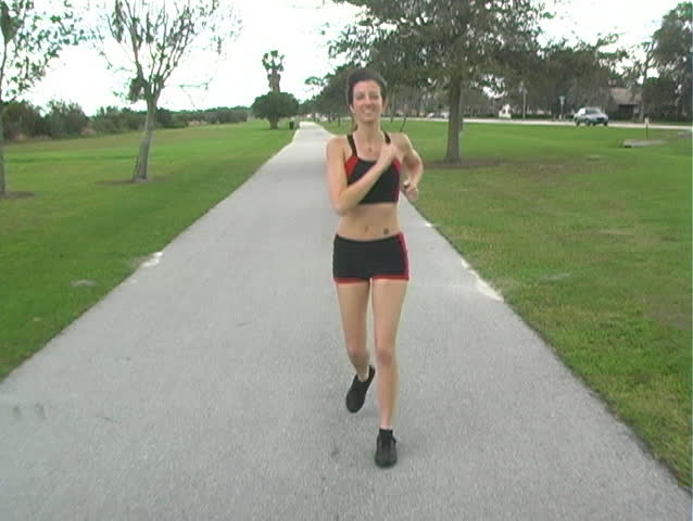 A beautiful young woman jogging outdoors toward the camera (full-length, tracking)