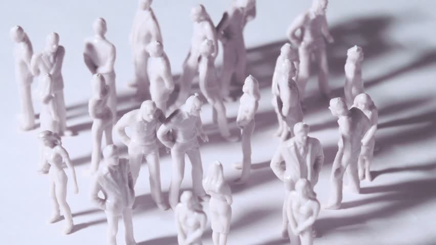 Group of little unpainted toy men and women stand and drop shadows, composition rotates, view from above