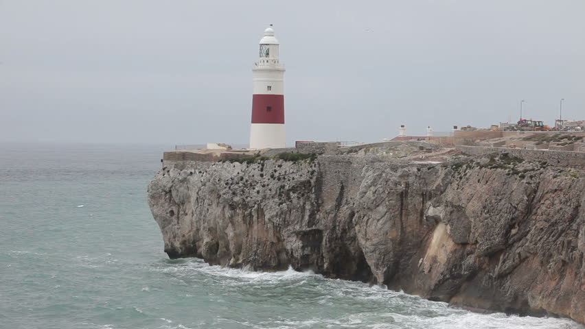 Lighthouse red and white on the tip of the Straights of Gibraltar, Europa Point. Mediterranean Sea ocean waves crashing against rock and cliff. Red and white lighthouse stands tall. 