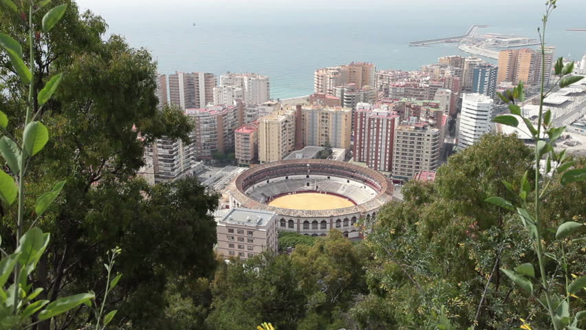 Bull ring city center Malaga, Spain. Historic round Colosseum with outdoor seats where the popular bull fighting is viewed. Tall building surround the arena near the Mediterranean Sea and coast line.