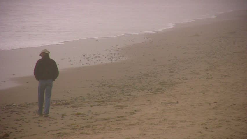 Man in a cowboy hat walking on a foggy beach in winter.