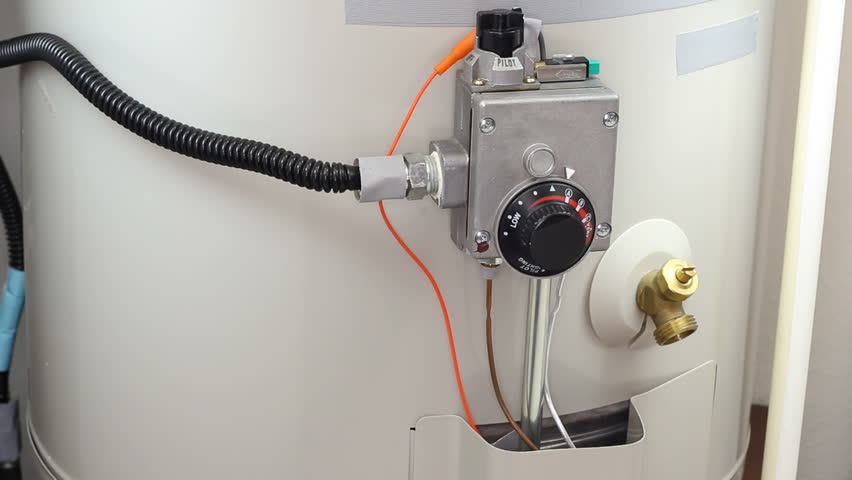 Hand of a man seen turning down house gas water heater temperature dial.