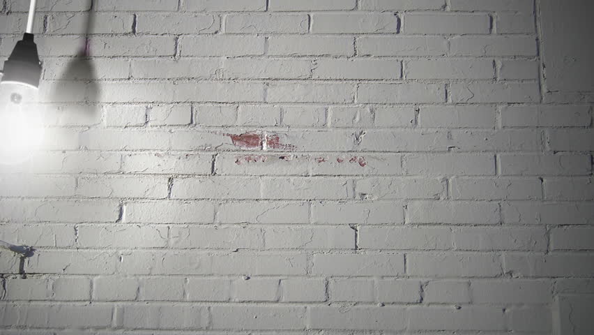 naked light bulb swinging against a white brick background 