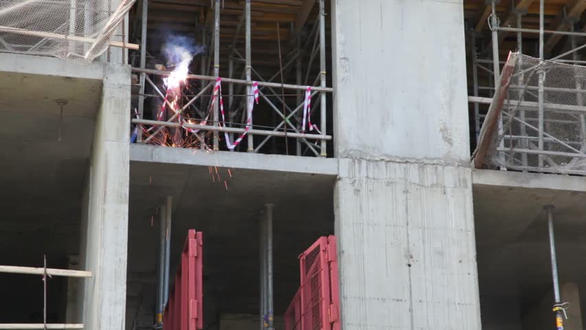 Worker weld metal railing by acetylene torch, he stand on second level view from below