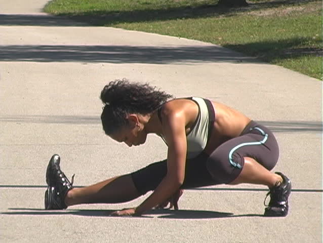 A beautiful woman stretches on a jogging track before running on a bright, sunny day.