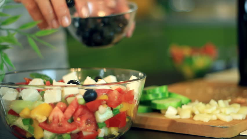 Female hands pouring oil into salad in glass bowl