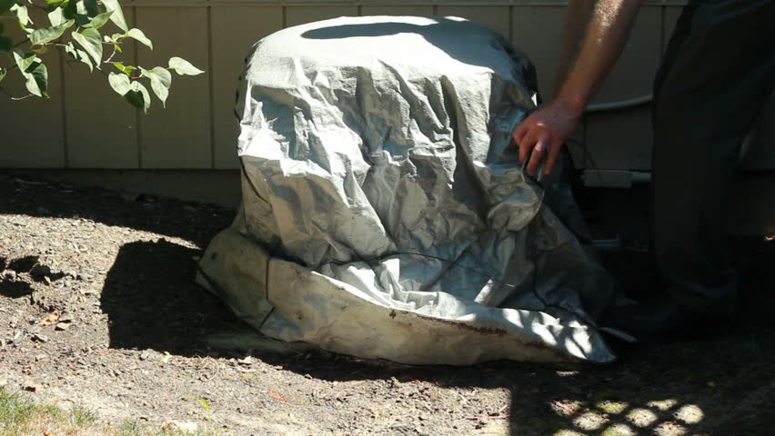 Man removing an air conditioner cover outside of his house on a sunny summer day.