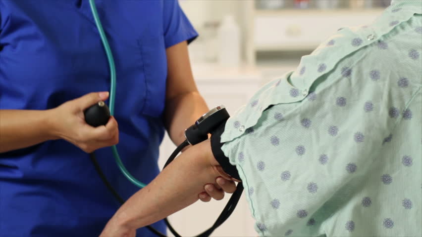 A lovely Hispanic nurse takes blood pressure reading from a mature female patient.