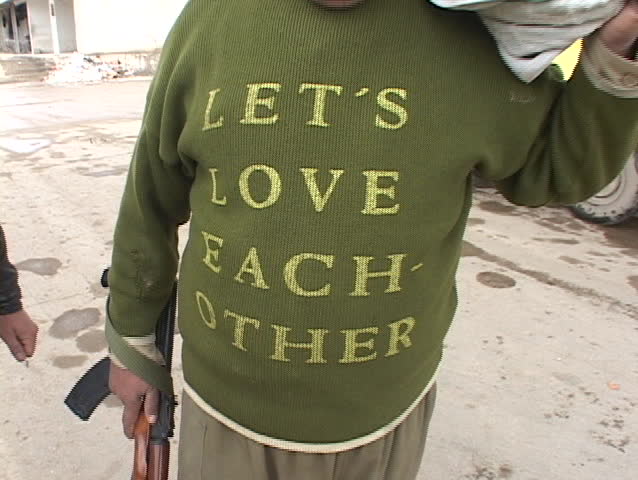 IRAQ - CIRCA 2003: An Iraqi man holding a rifle shows his shirt which says Lets Love Each Other circa 2003 in Iraq.