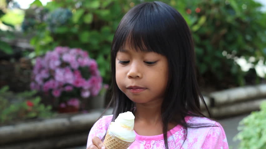 A cute little 5 year old Asian girl enjoys a delicious ice cream cone during the summer.
