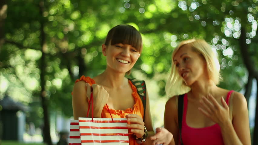 Happy young female friends with shopping bags in the park, camera stabilizer shot