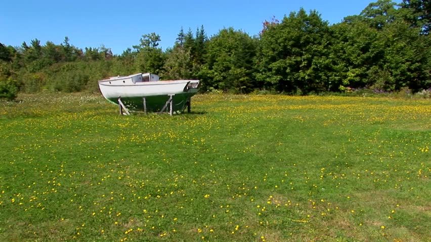 An old boat in Main, New England rests on wooden planks in the middle of a field.