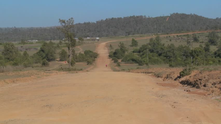 A man walks on a lonely dusty dirt road in Africa.