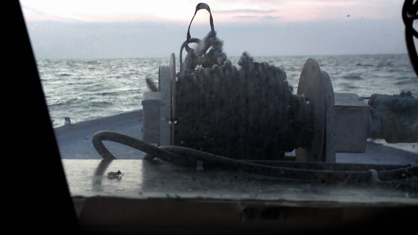 A rope is released into the water from the deck of a boat, as the captain sits at the controls.