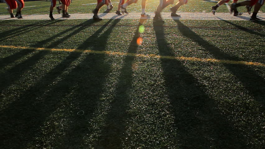 Players running past the frame with focus on their shadows during sundown.
