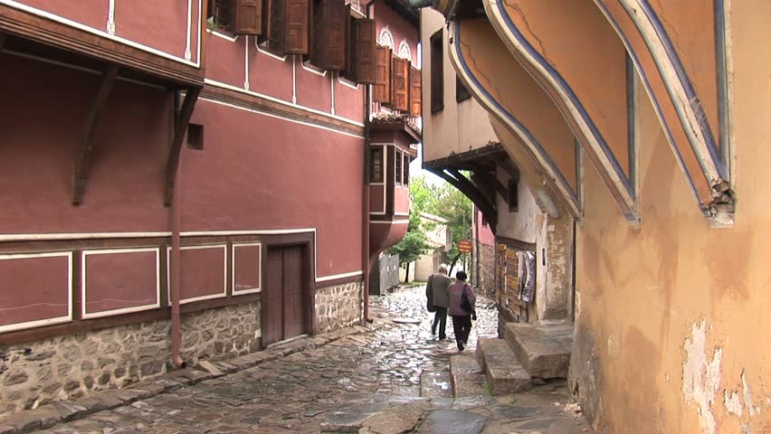 two people walking down an old street of plovdiv
