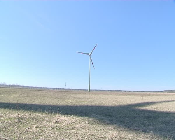Shadow of rotating windmill on ground and windmill in distance. 