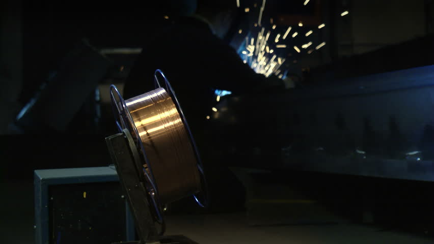 Men working in heavy industry using welding mask, tools and equipment on iron bar