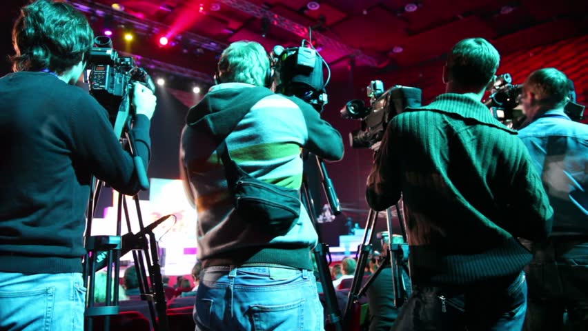 Operators on workplace in row of few cameras, view from behind on event