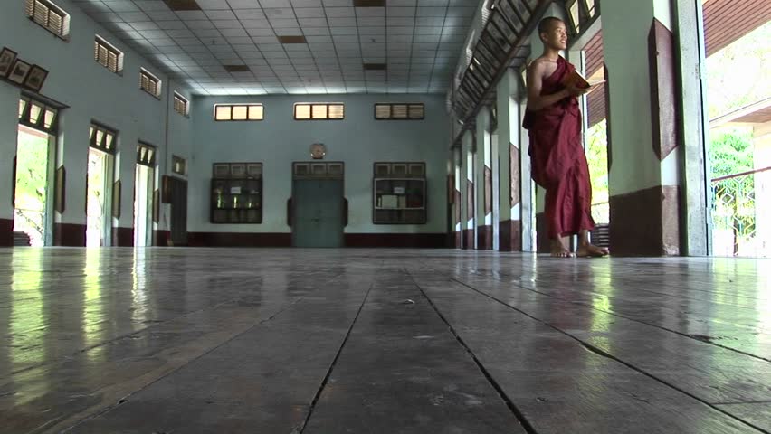 BURMA - CIRCA 2009: A Buddhist monk carries a book and gazes outside a door.
