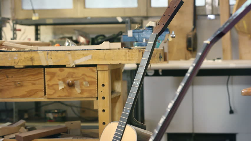 Young man at work as craftsman in italian workshop with guitars and musical instruments. Rack focus