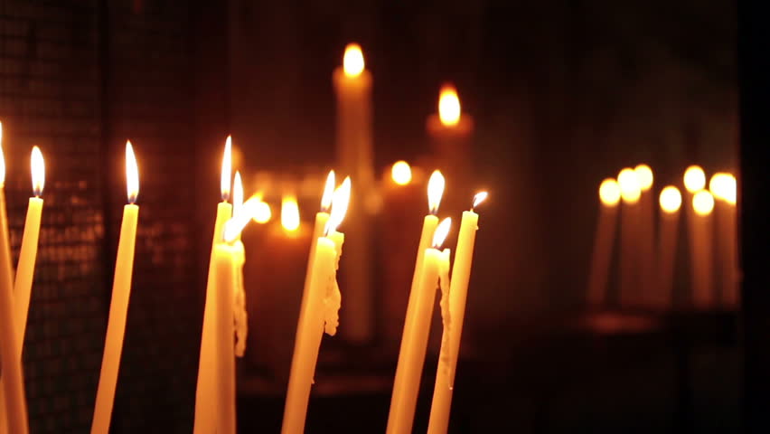 Prayer candles inside the Basilica Notre Dam de la Garde in Marseille France. Tall thin white candles in front of narrow DOF memorial plaques.  Bright yellow flames.