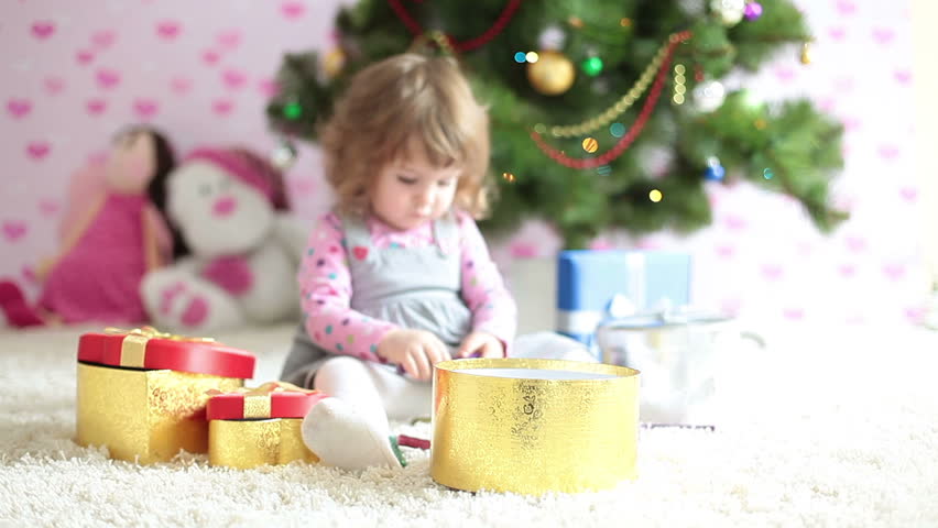 Baby girl shows tongue and sitting beside a Christmas tree 